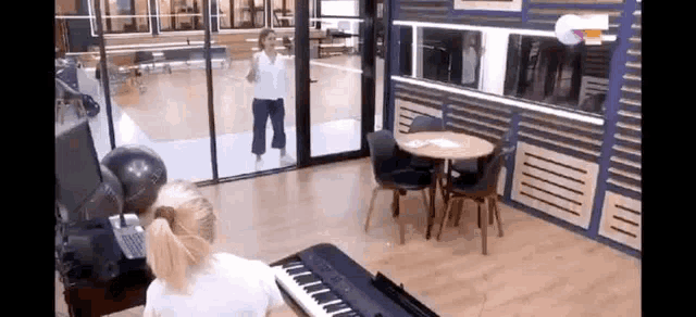 a woman is playing a piano in a room with a table and chairs in front of a glass door .