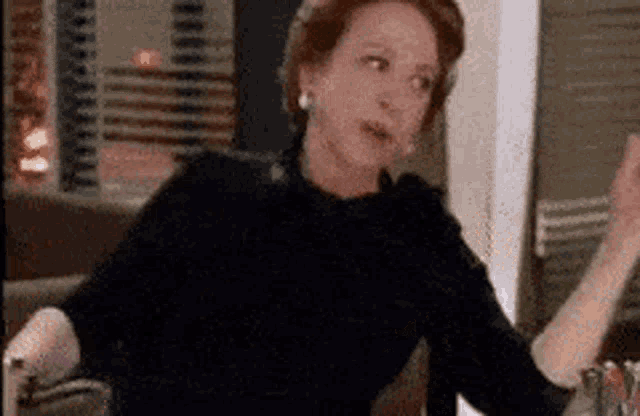 a woman in a black sweater is sitting at a table with her arms outstretched in front of a window .