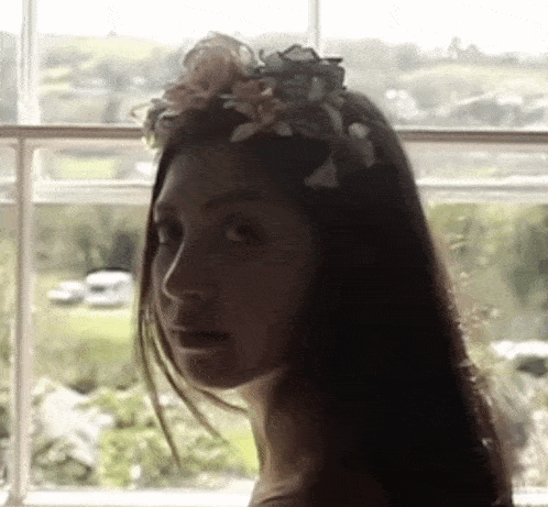 a woman with a flower crown on her head looks out a window .