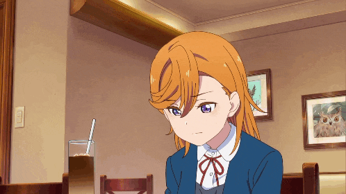 a girl with orange hair and blue eyes is sitting at a table with a picture of an owl on the wall behind her