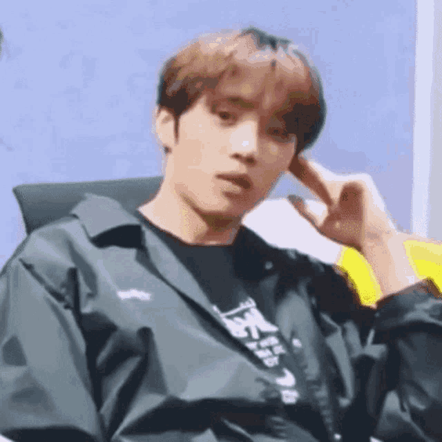 a young man is sitting in a chair with his hand to his ear and making a funny face .
