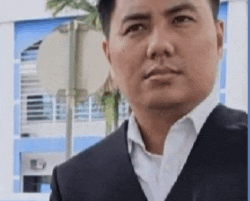 a man in a suit and white shirt is standing in front of a building looking at the camera .