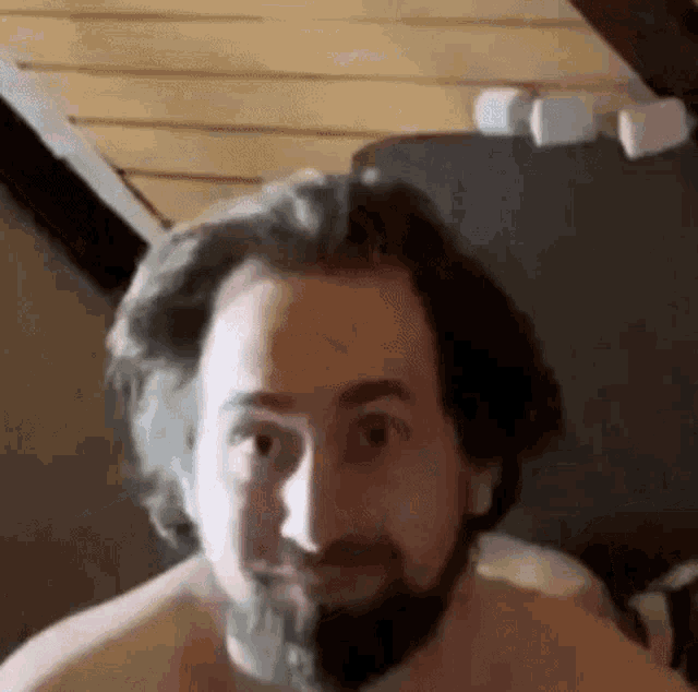 a shirtless man with a beard is making a funny face while looking at the camera .