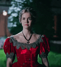 a woman in a red dress and necklace is standing in the grass at night .