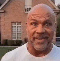 a bald man with a beard is smiling in front of a brick building .