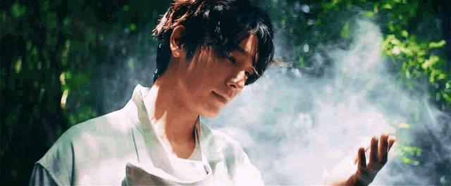 a man in a white shirt is standing in the woods holding something in his hand .