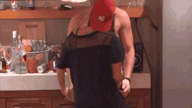 a man in a red ny hat is holding a woman in a black dress in a kitchen .