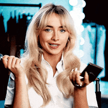 a blonde woman in a white shirt is holding a brush and a mirror .