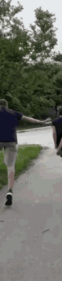 two men are running down a path holding hands .