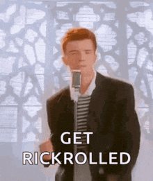 a man in a suit is singing into a microphone with the words get rickrolled written below him .