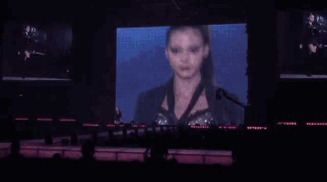 a woman is standing in front of a large screen on a stage in front of a crowd .