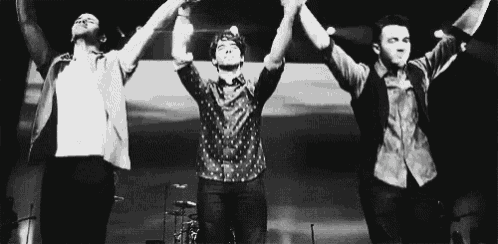 a black and white photo of three men holding hands in the air .
