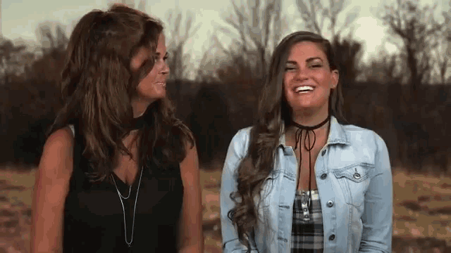 two women standing next to each other in a field laughing .