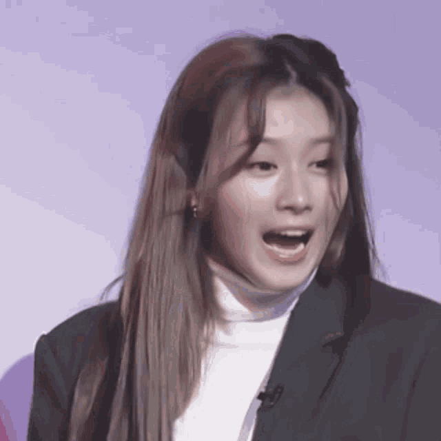 a close up of a woman wearing a black jacket and a white turtleneck with her mouth open .