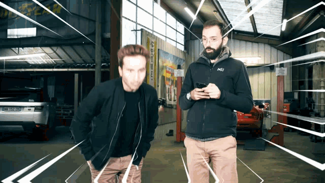 two men standing in a garage with one wearing a jacket that says millet
