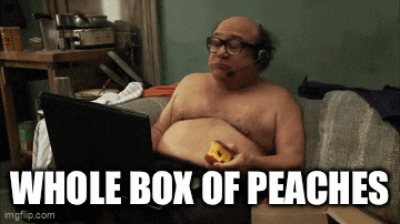 a shirtless man sits on a couch with a laptop and a whole box of peaches below him