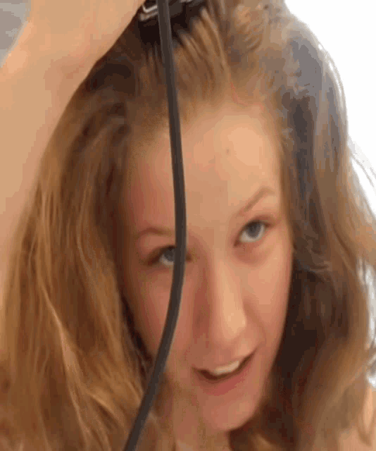 a close up of a woman 's face with a black cord hanging from her hair