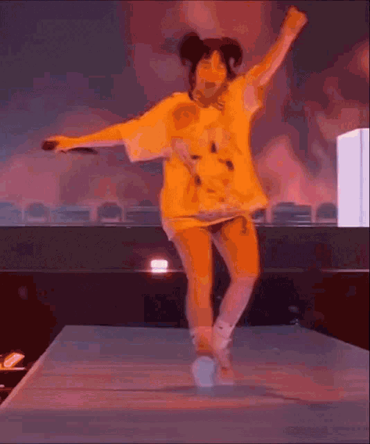 a woman is jumping in the air on a stage while wearing a yellow shirt .