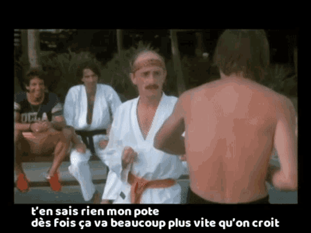 a man without a shirt is standing in front of a group of men in karate uniforms