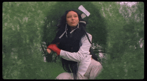 a woman with long black hair and red gloves is kneeling in the grass .