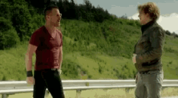 two men are standing next to each other on a highway and talking .