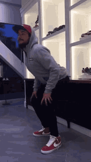 a man wearing a hat and a hoodie is standing in a shoe store .