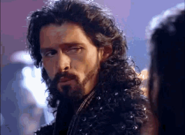 a man with long hair and a beard is looking at a woman in a dark room .