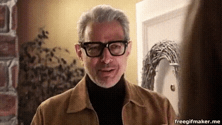 a man wearing glasses and a brown jacket is standing in a room .