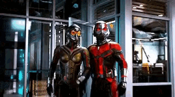 two ants in superhero costumes are standing next to each other in front of a building .