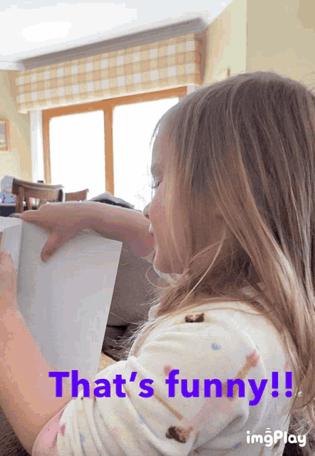 a little girl is holding a piece of paper with the words that 's funny below her