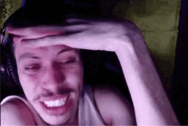 a man wearing headphones is covering his face with his hand and smiling .