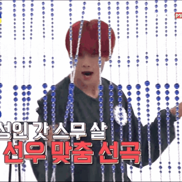 a boy with red hair is standing in front of a curtain with blue beads