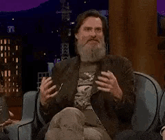 a man with a beard is sitting on a couch with the word disgrace written in yellow letters