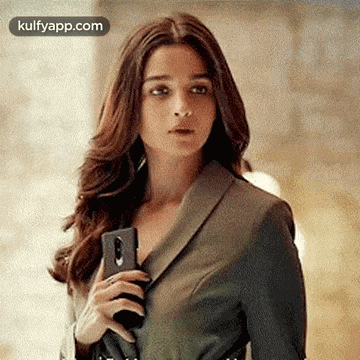 a woman in a suit is holding a phone in her hand .