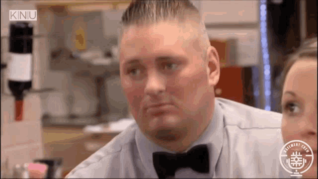 a man in a bow tie is looking at a woman in a kitchen .