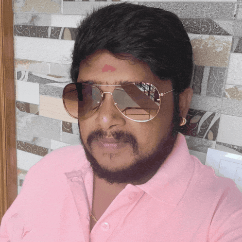 a man wearing sunglasses and a pink shirt has a red spot on his forehead