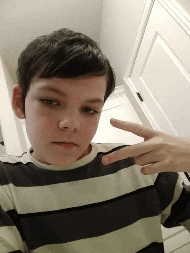 a young boy in a black and white striped shirt is giving a peace sign