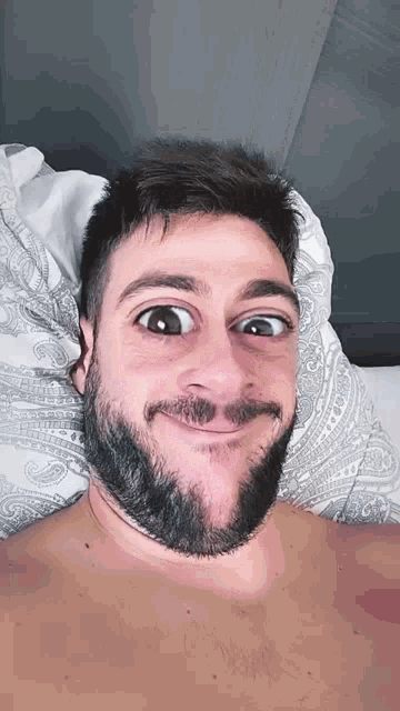a shirtless man with a beard is making a funny face while laying in bed