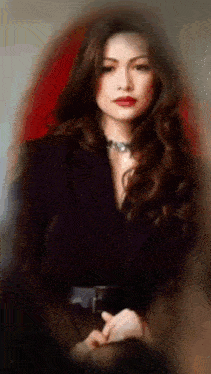 a woman in a black jacket and necklace is standing in front of a red wall .