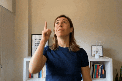 a woman in a blue shirt holds her finger up in front of a sign that says " quand "