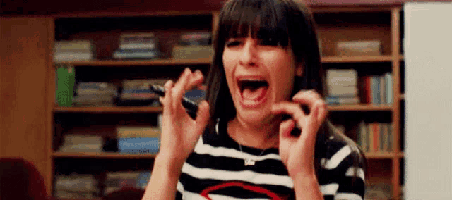 a woman in a striped shirt is screaming and holding a cell phone in her hand .