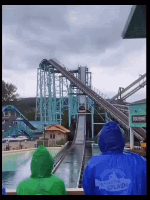 a man wearing a blue jacket that says submarine splash watches a roller coaster