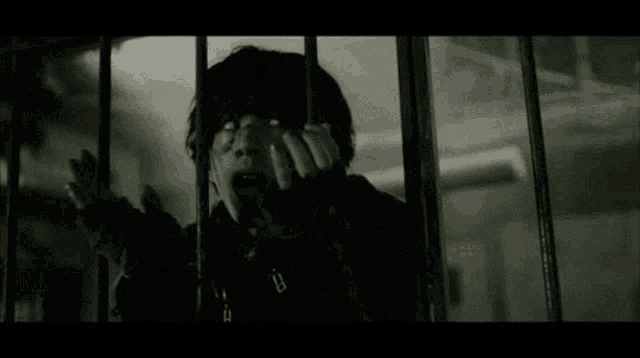 a person is behind bars and covering their face with their hand .