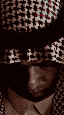 a man wearing a head scarf and a hat looks down