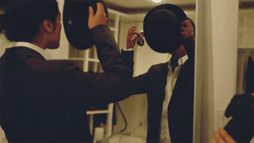 a man in a suit is adjusting his hat in a mirror