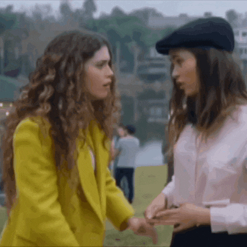 a woman in a yellow jacket and a woman in a pink shirt are holding hands and talking to each other .