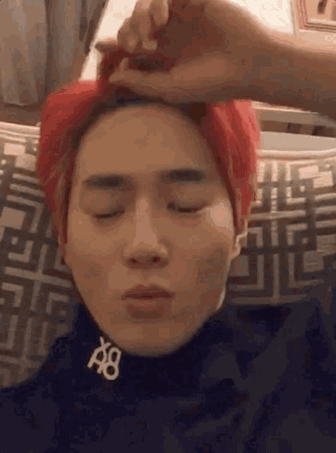a man with red hair is laying on a couch with his eyes closed and a person is touching his hair .