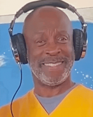 a man wearing headphones and a yellow shirt smiles
