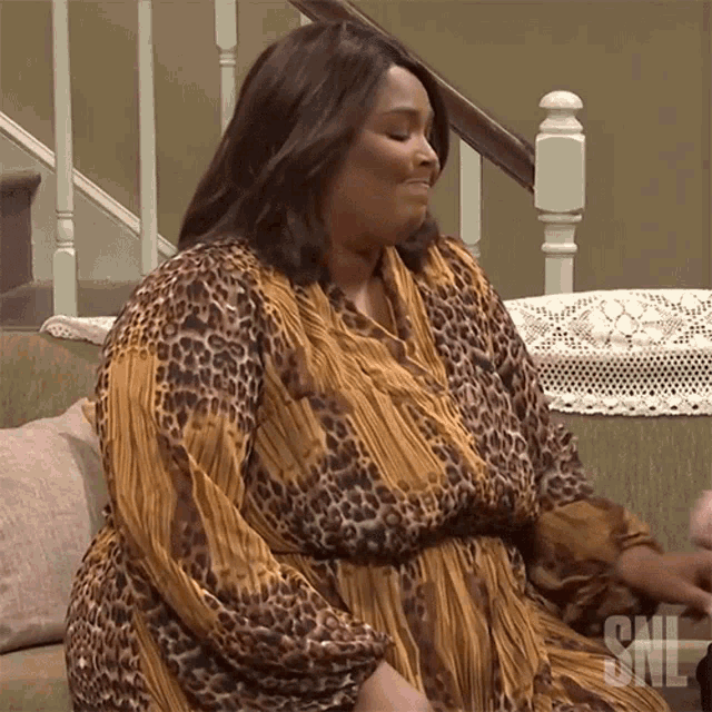 a woman in a leopard print dress sits on a couch with the snl logo