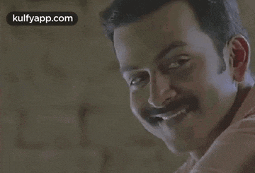 a man with a mustache is smiling while looking over his shoulder .
